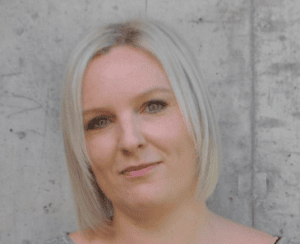Bilde av en kvinne med blond hår foran en betongvegg, representerer pålitelighet og kundeservice i bussbransjen.